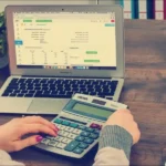 Kalkulator i laptop z arkuszem kosztów na biurku, liczenie kosztu zespołu QA