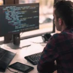 Tester przy biurku z monitorami pełnymi kodu, najlepsi testerzy nie byli najlepsi technicznie