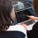 Dwoje specjalistów QA dyskutuje nad kodem przy laptopie podczas szkolenia z testowania oprogramowania