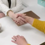 Uścisk dłoni nad białym biurkiem z notatnikiem i filiżanką, rozmowa o budżecie na zespół QA