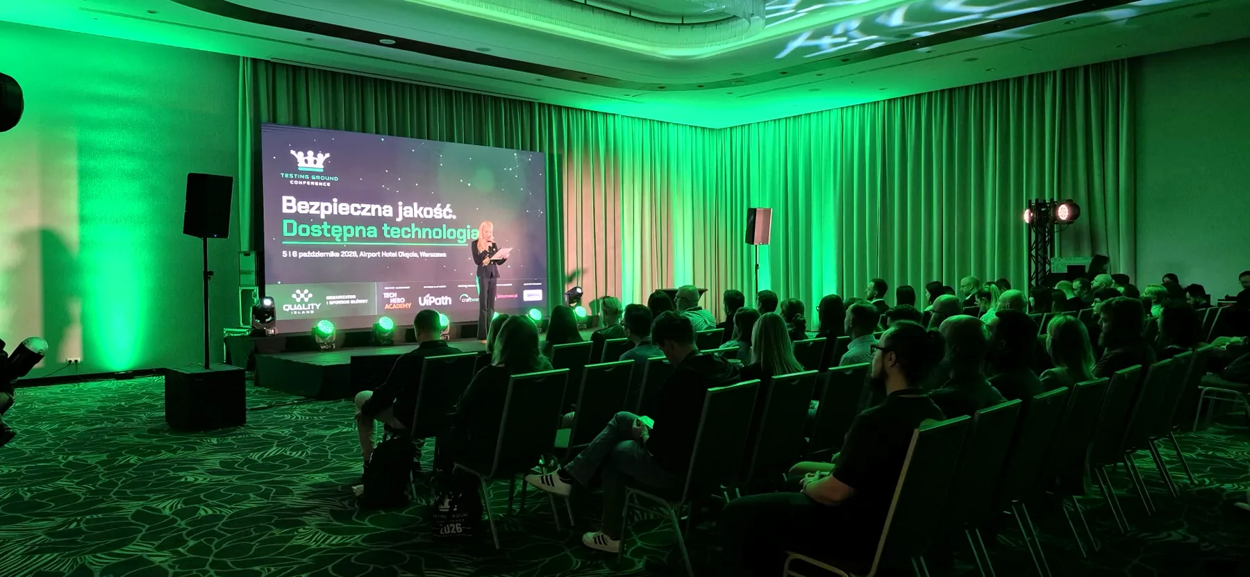 Pełna sala Testing Ground Conference 2026, na ekranie hasło Bezpieczna jakość. Dostępna technologia